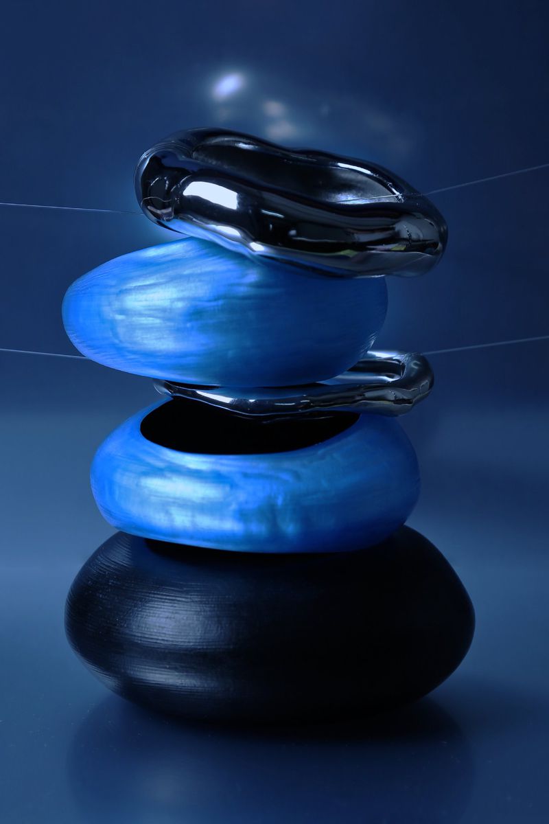 Stack of black, silver, and blue decorative stones. The polished stacked stones are set against a glossy blue background in a studio.