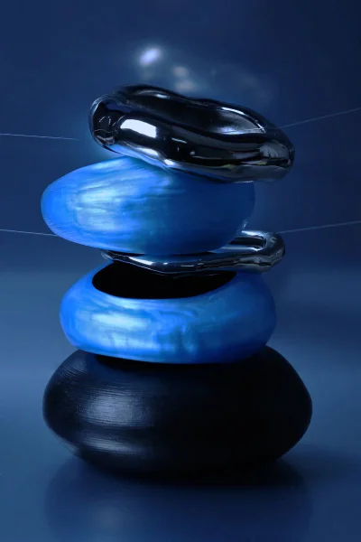 Sculptural Alexis Bittar bangles in electric blue resin, polished chrome, and matte black stacked against a deep blue background.