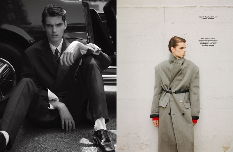 Monochrome portrait of a man in a suit seated next to a vintage car; another man stands in a coat against a white wall.