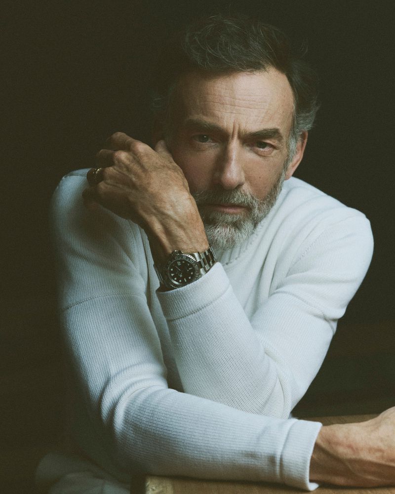 Portrait of an adult man with a beard wearing a white sweater and a watch, captured in a studio with controlled lighting.