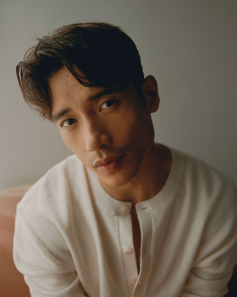 Portrait of an adult male with dark hair wearing a cream-colored button-down shirt, gazing slightly downward in an indoor setting.