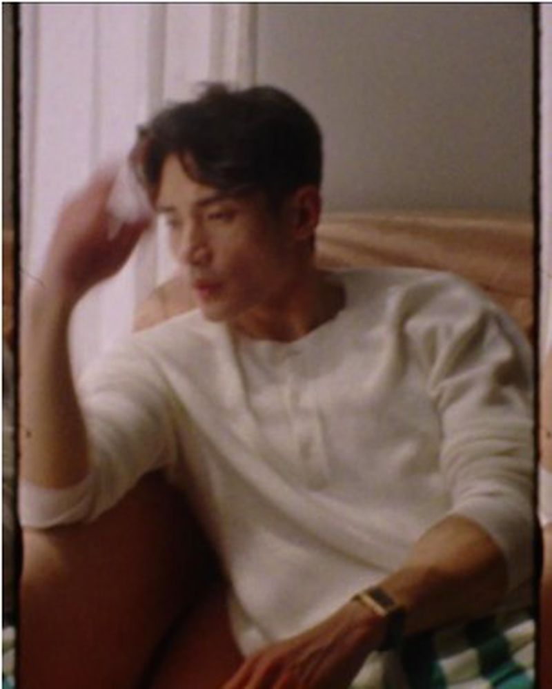 Adult male sits indoors in casual shirt, captured in medium shot with soft, neutral lighting highlighting his thoughtful, relaxed pose.