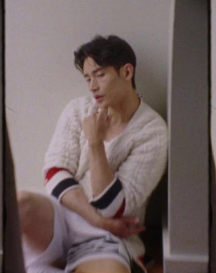 Actor Manny Jacinto seated against a plain wall wearing a cream cable-knit cardigan with striped cuffs for InStyle U.S.