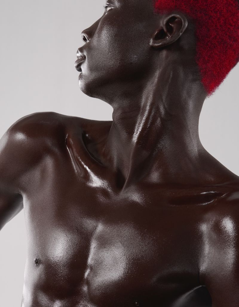 Close-up studio shot of an adult male with brown skin and red hair looking up. The subject is shirtless against a neutral background.