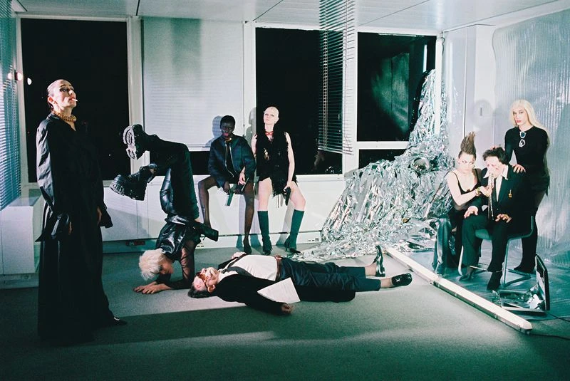 Indoor fashion editorial shot of a group of adults in dark clothing with diverse poses in a modern interior with windows and props.
