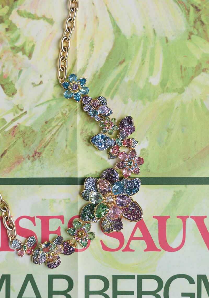 Close-up of a gold chain necklace with colorful flower embellishments on a pale yellow background with green and red text.