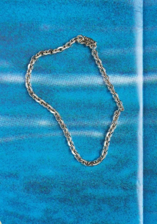 Silver chain link necklace with a triangle logo clasp displayed on a vibrant blue textured background.