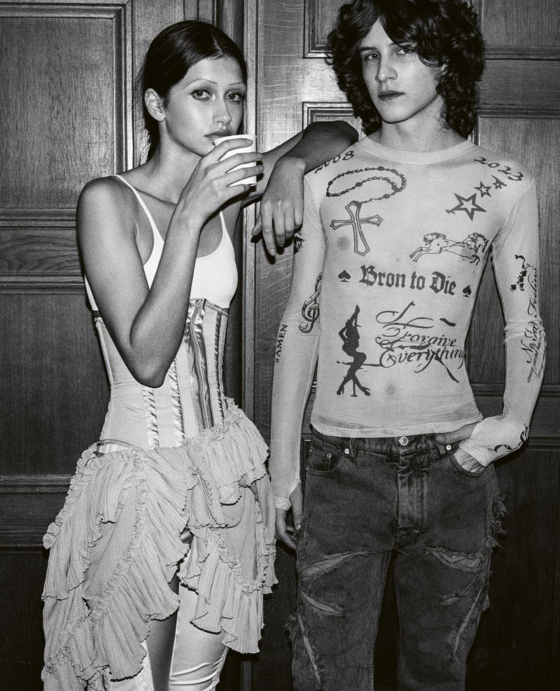 Black and white shot of a stylish adult female sipping from a cup while standing next to an adult male in a sheer, long-sleeved shirt.