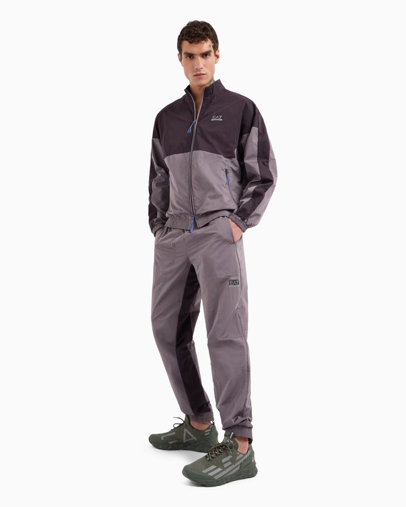Male model in a two-tone tracksuit and olive sneakers poses in a full shot against a white background, showcasing athletic wear.