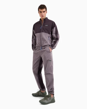 Male model in a two-tone tracksuit and olive sneakers poses in a full shot against a white background, showcasing athletic wear.