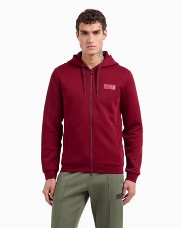 Male model wearing a burgundy zip-up hoodie and green sweatpants against a white background for Emporio Armani EA7