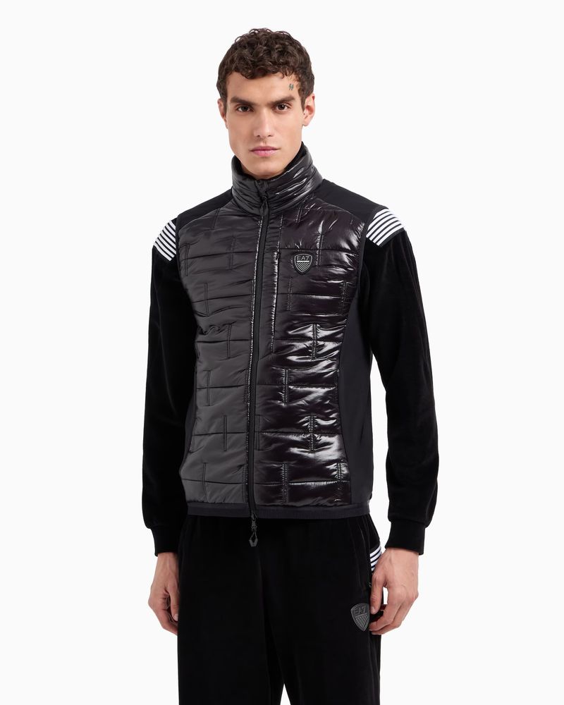 Male fashion model poses in a black EA7 Emporio Armani quilted jacket and matching pants on a white backdrop in a studio shot.
