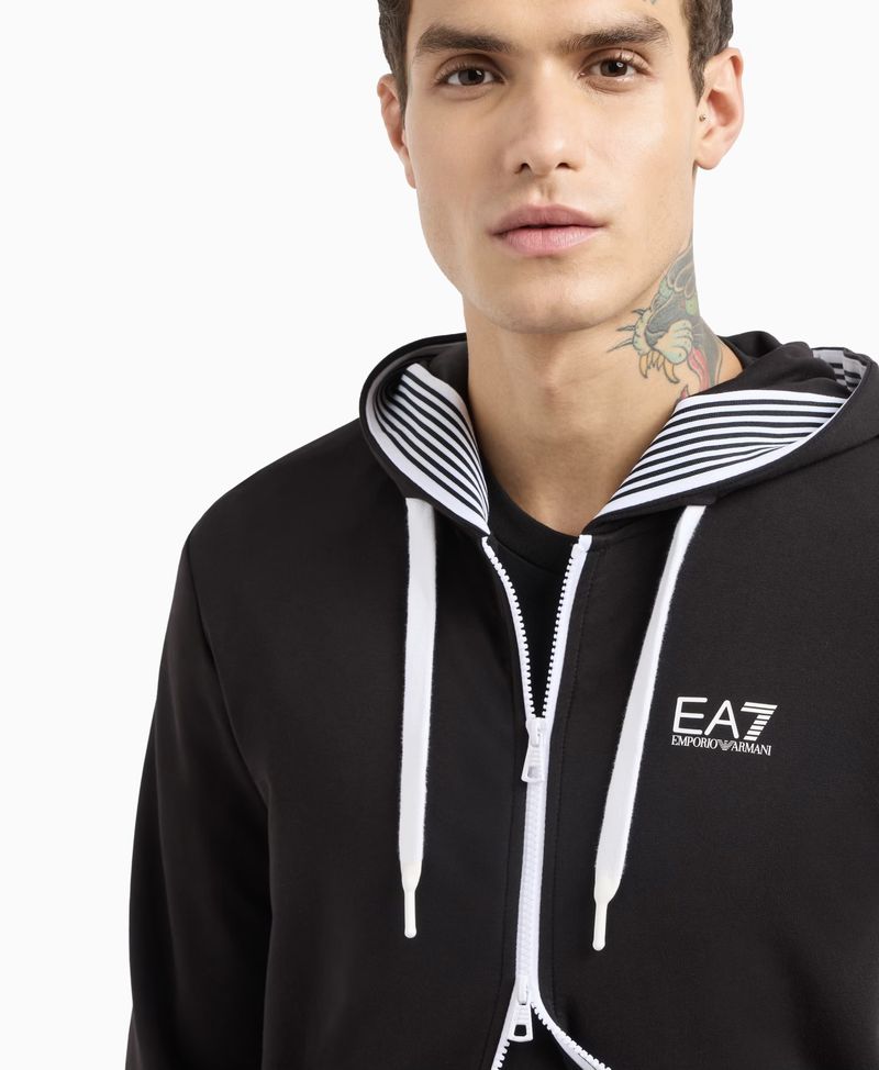 Close-up of a brunette adult male wearing a black EA7 Emporio Armani zip-up hoodie against a white background in a studio shot.
