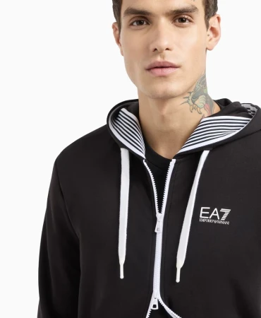 Close-up of a brunette adult male wearing a black EA7 Emporio Armani zip-up hoodie against a white background in a studio shot.