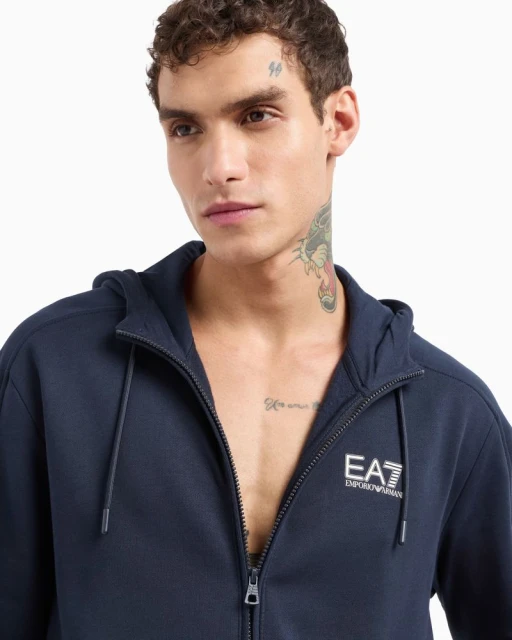 Close-up of an adult male wearing a navy-blue zip-up hoodie, showcasing the EA7 Emporio Armani logo against a plain white background.