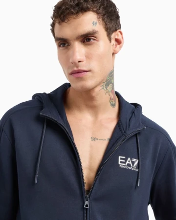 Close-up of an adult male wearing a navy-blue zip-up hoodie, showcasing the EA7 Emporio Armani logo against a plain white background.