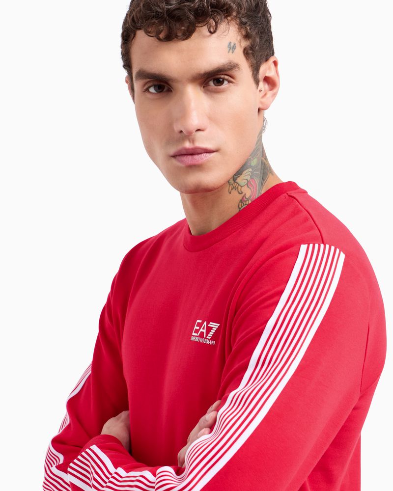 Close-up of an adult male wearing a red long-sleeved shirt with white stripes on the sleeves against a white backdrop.
