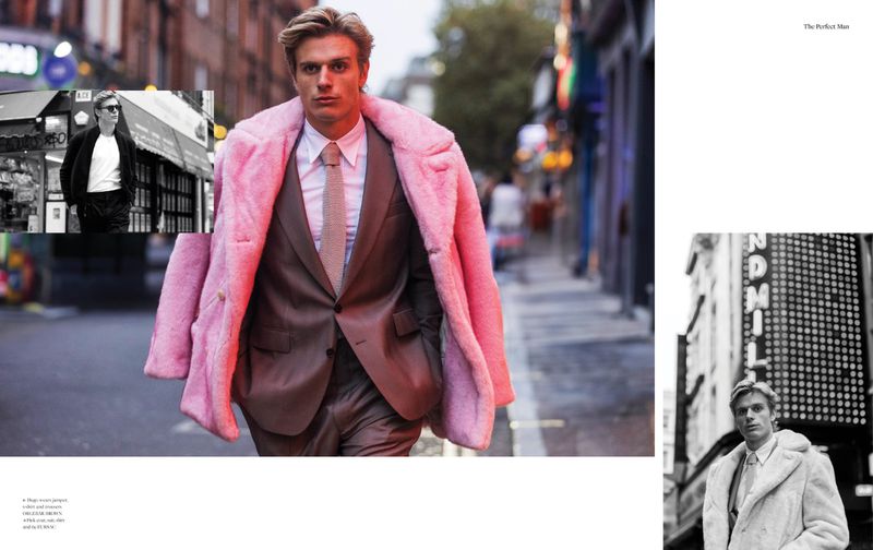 Fashion editorial shot of a male model wearing a brown suit with a pink faux fur coat on a city street with blurred pedestrians.