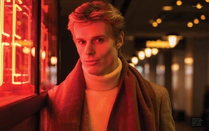 Man wearing a cream turtleneck sweater and brown scarf under red neon lighting for The Perfect Man Magazine