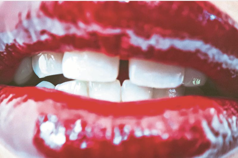 Macro shot of an adult female's red glossy lips and white teeth. Close-up view of vibrant makeup and dental features.