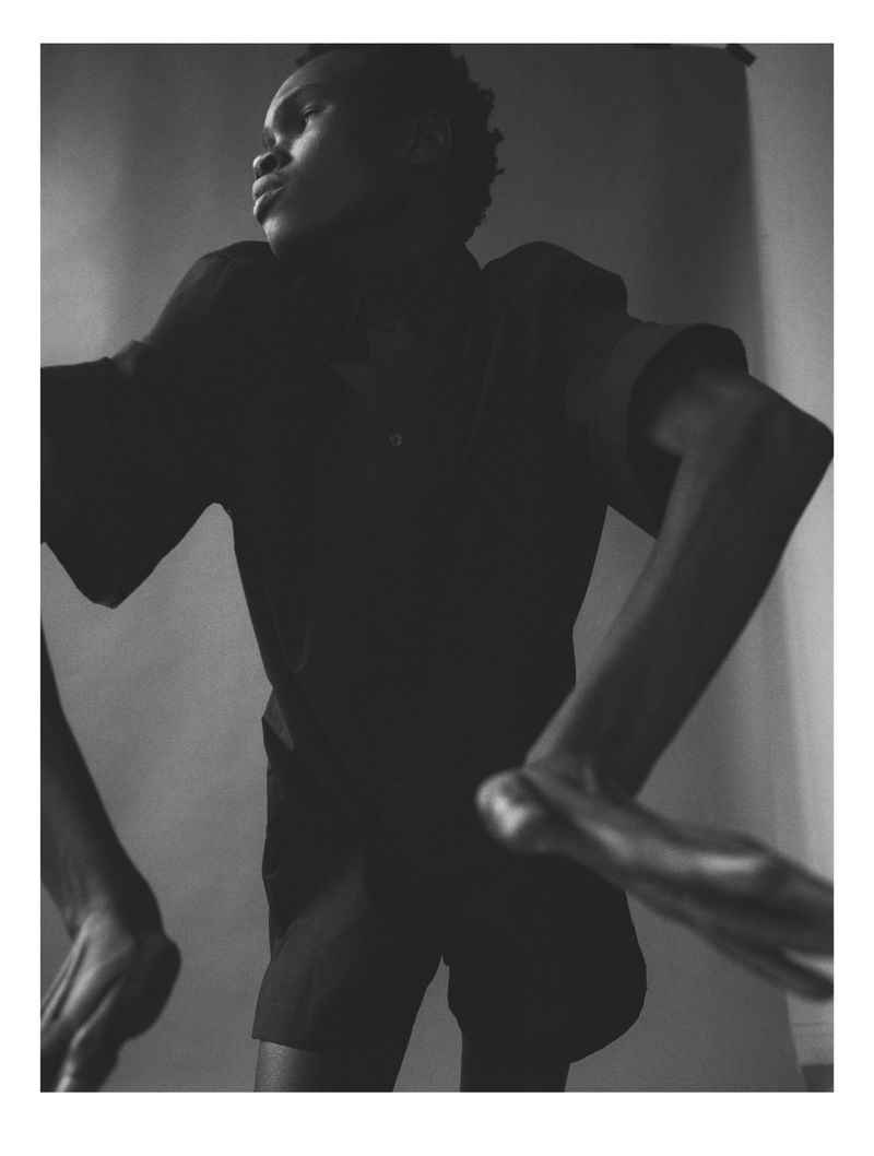 Monochrome portrait of a Black man in a dark shirt with a neutral expression, captured in a studio setting against a plain backdrop.