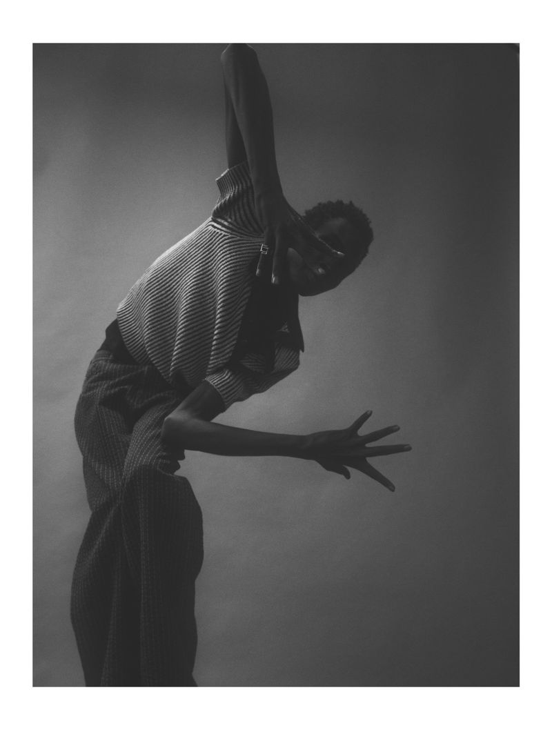 Portrait of an adult in motion, captured in a high-contrast black-and-white studio photograph with a neutral backdrop, full-length pose.