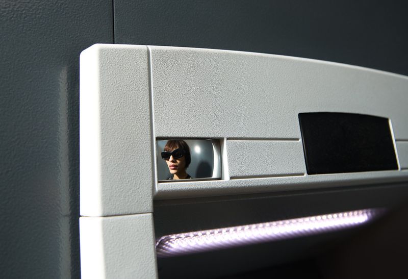 An adult looking out from a square opening in a white wall wears sunglasses, illuminated by a light strip below in an indoor scene.