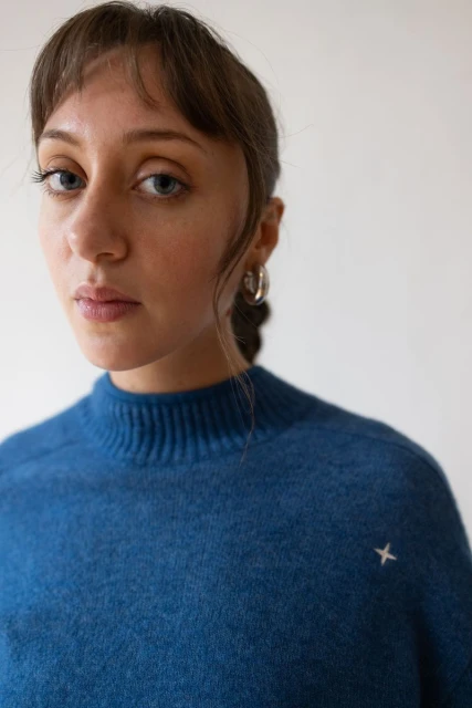 Close-up portrait of a young woman with light skin and blue eyes wearing a blue sweater against a plain white background in a photo studio.