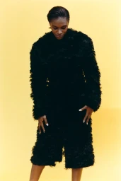 Black woman wearing a textured black coat against a solid yellow studio background