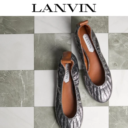 Two silver ballet flats are displayed on a checkered tile background in a studio shot for a fashion or shoe advertisement.