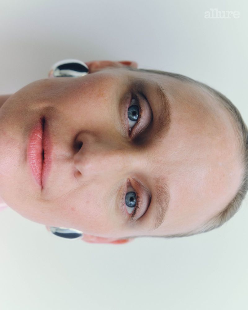 Close-up portrait of an adult woman with blue eyes and a light complexion, wearing silver earrings, against a white background.