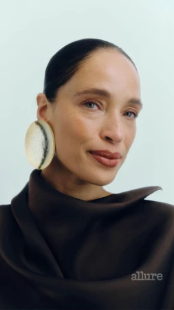 Close-up of an adult woman with dark hair and brown top wearing large round earrings against a light background. Beauty shot.