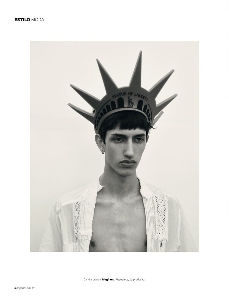Portrait of a person wearing a Statue of Liberty headpiece and a white shirt against a neutral background in a studio fashion shot.