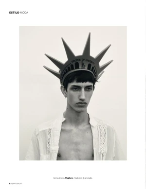 Monochrome portrait of a male model wearing a Statue of Liberty spiked crown headpiece and a white lace shirt against a plain background.