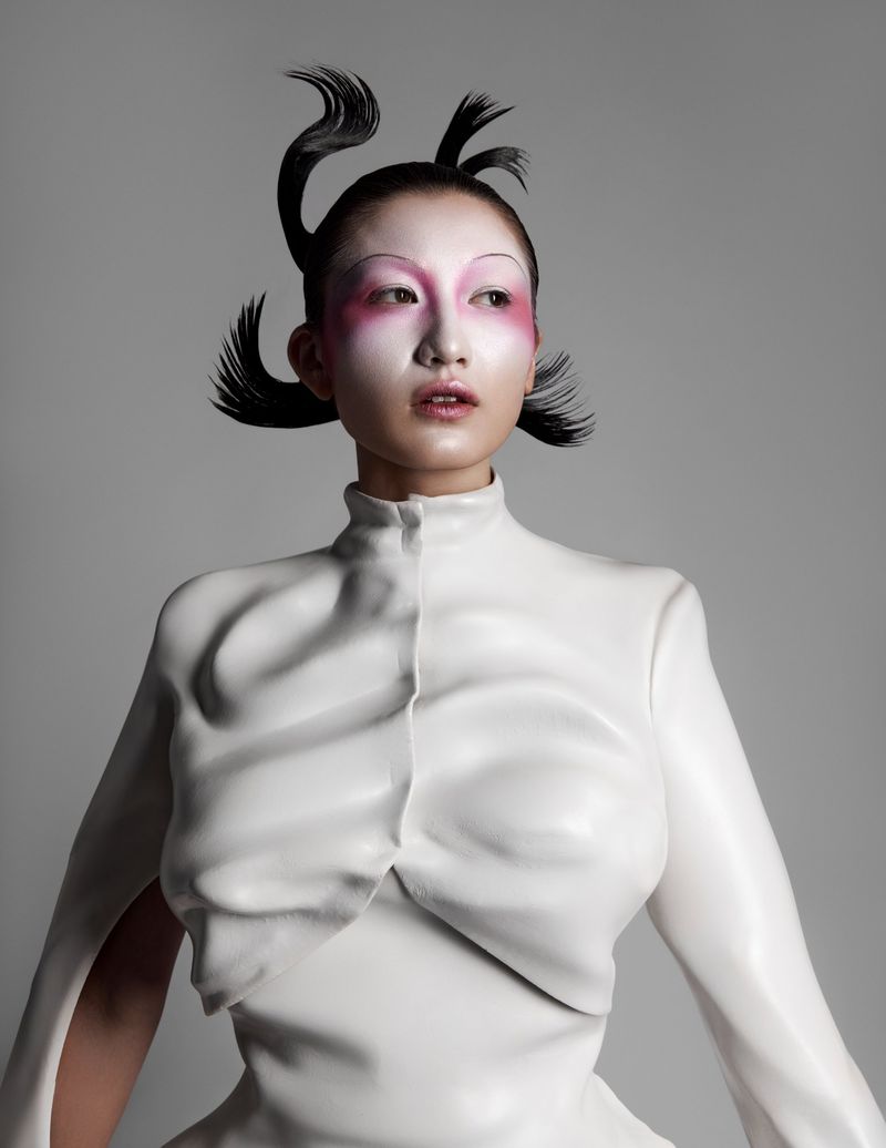 Asian woman with avant-garde hair and makeup wearing a white textured dress in a studio setting, fashion-forward and artistic.