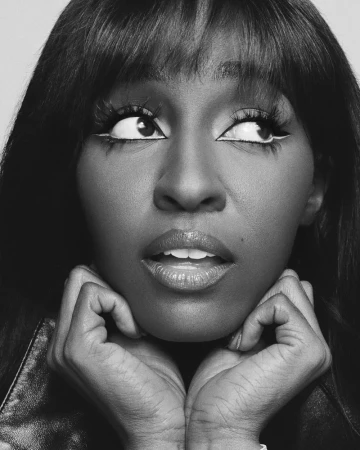 Black and white portrait of a Black woman with long dark hair and dramatic eye makeup looking up with hands near her face.