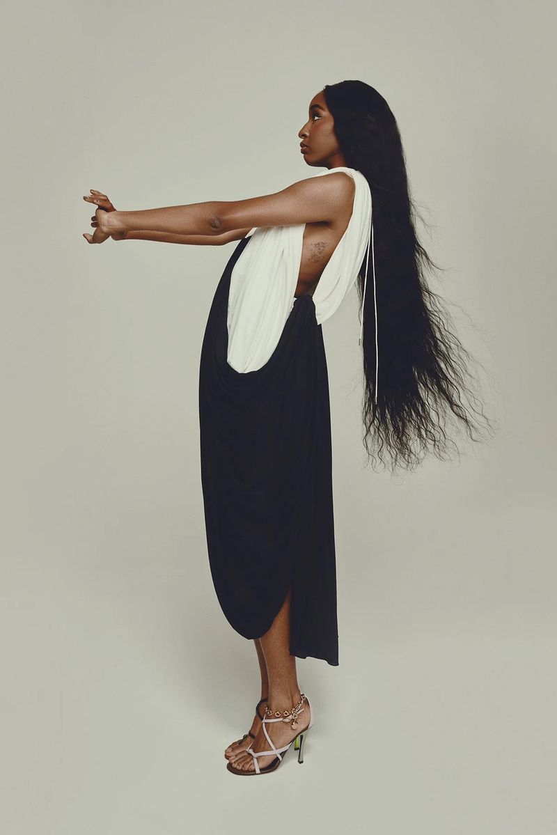 Elegant portrait of an adult female with long dark hair, wearing a stylish black and white dress and high heels, posing in studio.