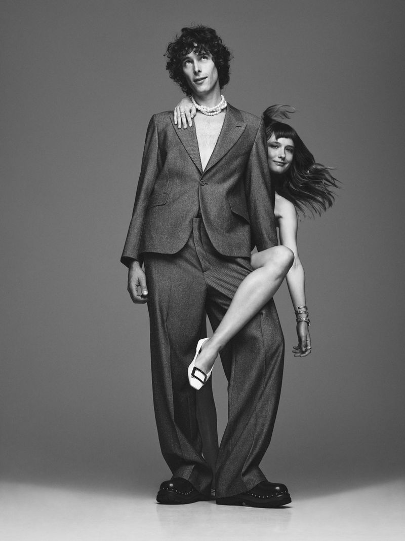 Monochrome portrait of a stylish adult couple posing in a photo studio. The male wears a suit, while the female rests her leg on him.