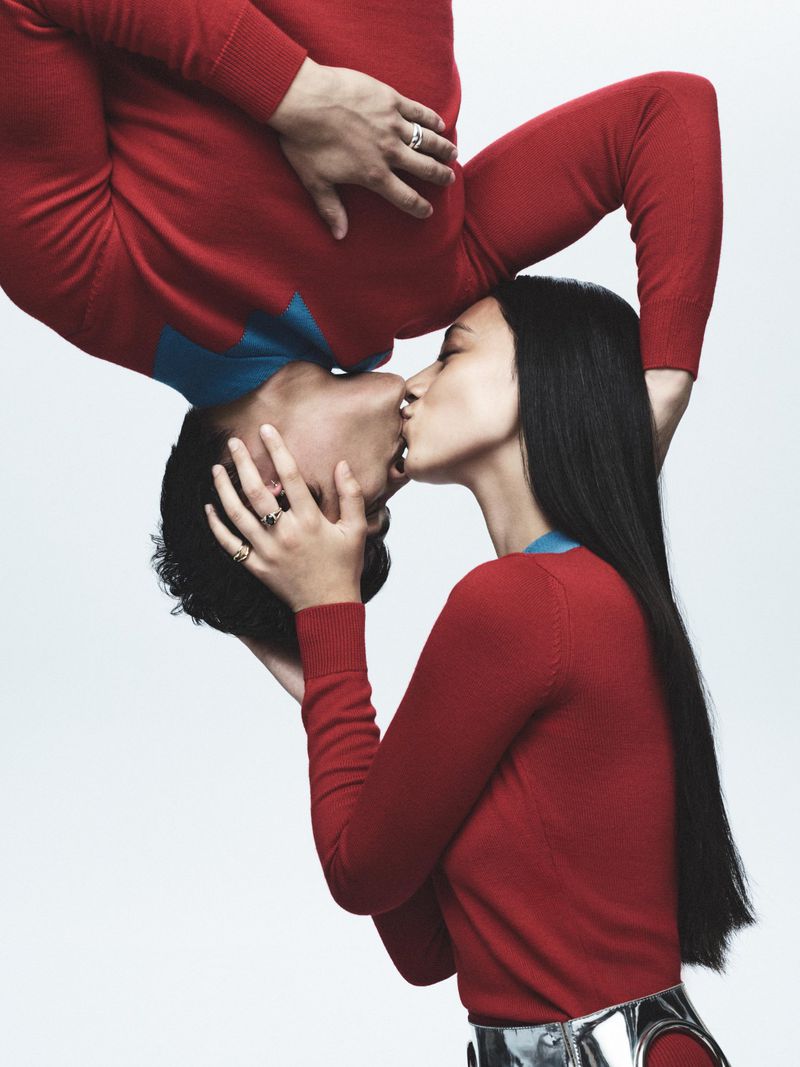 Upside-down view of a couple kissing, wearing red sweaters with blue accents on a white backdrop, showcasing a modern and intimate moment.