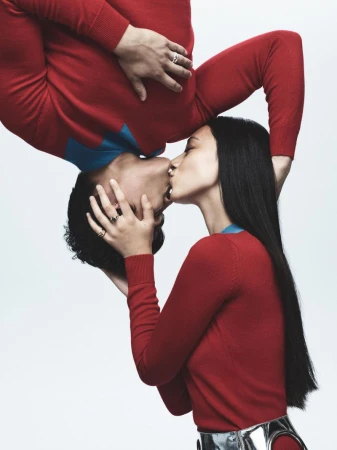 Upside-down view of a couple kissing, wearing red sweaters with blue accents on a white backdrop, showcasing a modern and intimate moment.