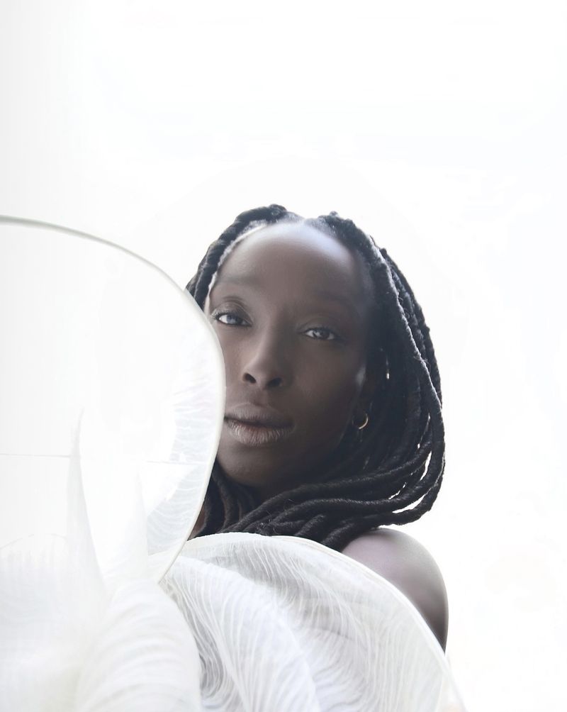 Elegant close-up studio portrait of a sophisticated African-American woman with box braids, draped in sheer white fabric against a clean white backdrop.