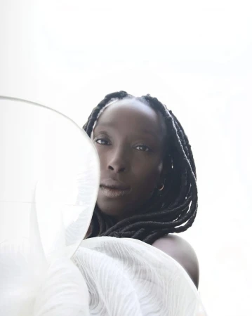 Elegant close-up studio portrait of a sophisticated African-American woman with box braids, draped in sheer white fabric against a clean white backdrop.