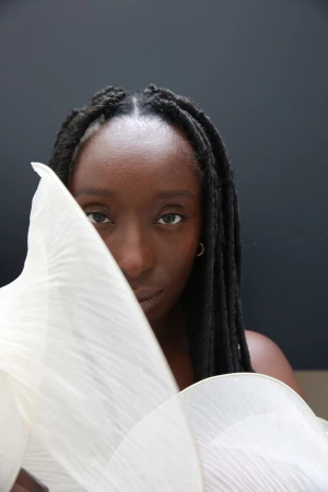 Portrait of Black woman with long braids partially obscured by large white fan-shaped structured accessory