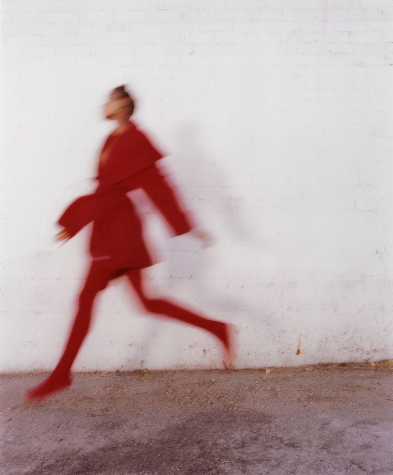 Blurred motion shot of a person in a red outfit running against a white wall in a studio setting, capturing a sense of movement.