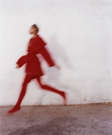 Blurred motion shot of a person in a red outfit running against a white wall in a studio setting, capturing a sense of movement.