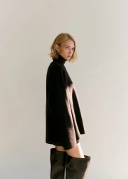 Model in dark turtleneck sweater and tall boots posing against a neutral white studio background