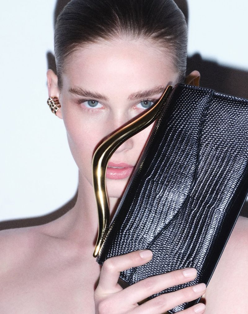 Close-up of a fashionable woman holding a black snakeskin clutch with a gold handle, showcasing beauty and high-end fashion accessories.
