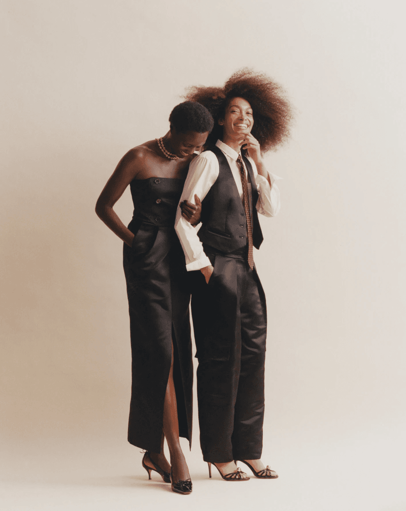 Two fashion models posing together against a neutral studio background for J. Crew in tailored black garments.