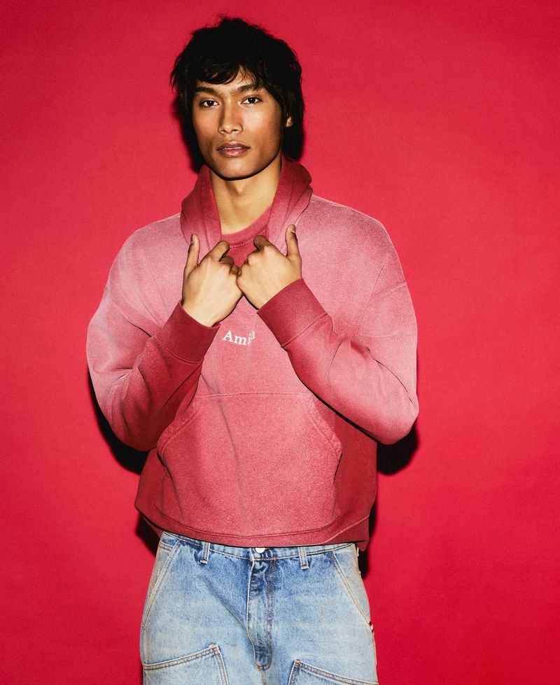 Portrait of a young man wearing a red ombre hoodie and jeans against a red backdrop in a studio setting with soft, even lighting.