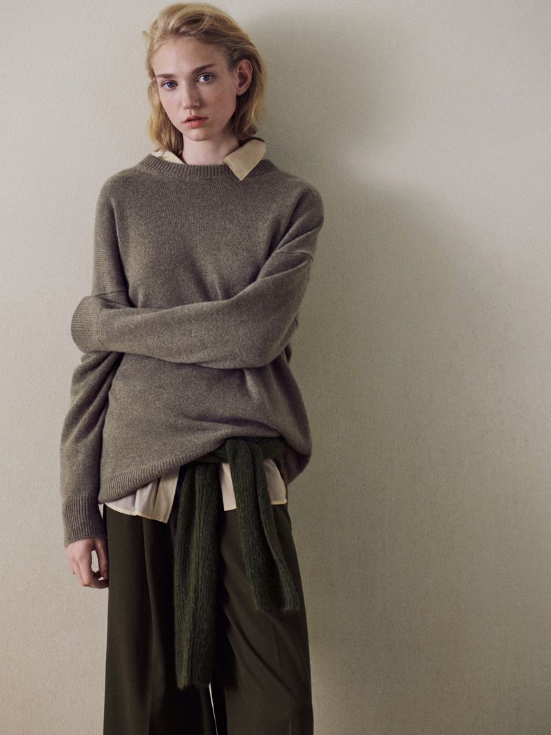 Model Tess Breeden posing in an oversized taupe cashmere sweater and dark olive trousers against a neutral studio backdrop.